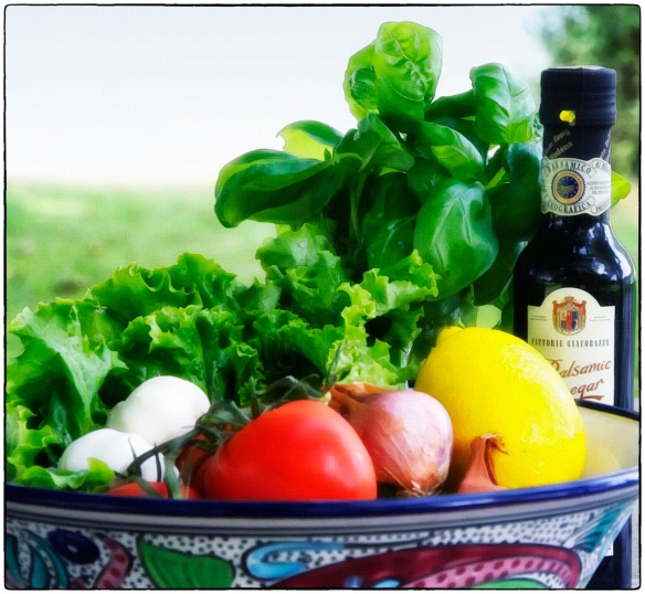 In the box: leafy lettuce, basil, bottle of wine, large basket, balsamic vinegar, patterned serving bowl, tomatoes, garlic, shallots, box of spaghetti, wooden spoon